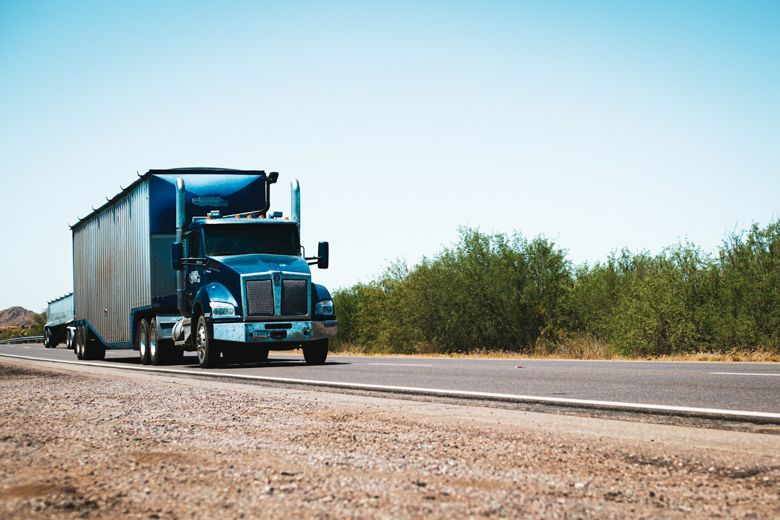 A semi truck driving down the road in the desert, trucking