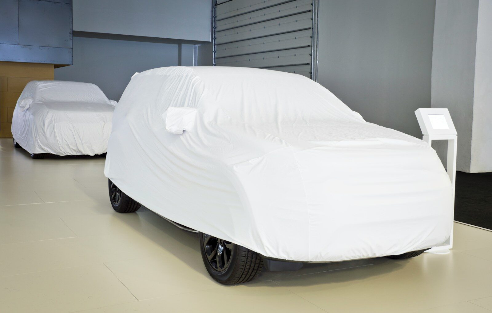 Two cars covered in white sheets indoors